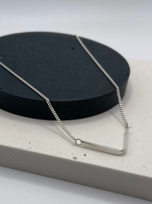 Silver arc shaped necklace on a black circluar display plate